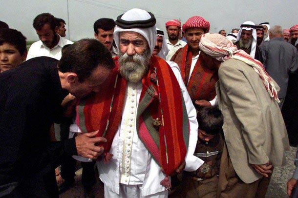 'Parade of the Sanjak': A sacred ancient brass peacock lamp representing Taws Melek is carefully wrapped in wool fabric and carried in procession by a mir as Yezidi laity offer their respects.